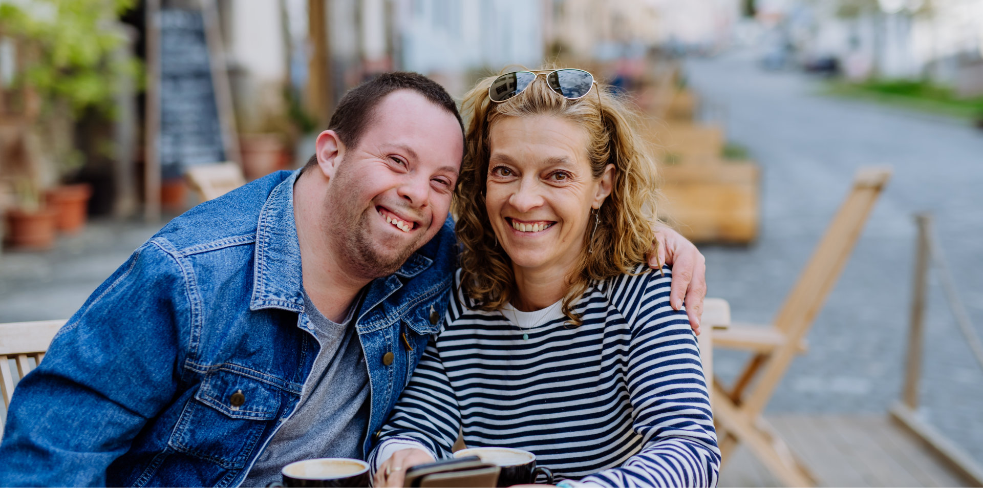 happy young man with Down syndrome with his mother sitting in cafe outdoors and talking